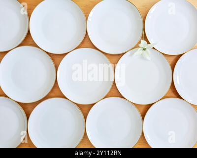 Des assiettes blanches vides se tiennent côte à côte sur une table en bois, une fleur de cornouiller blanche est disposée entre les assiettes comme décoration Banque D'Images