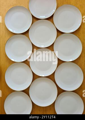 Assiettes blanches vides disposées les unes à côté des autres sur une table en bois comme un motif et photographiées d'en haut Banque D'Images