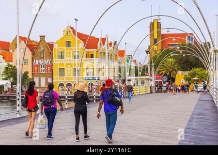 Touristes marchant à travers l'emblématique pont Queen Emma à Willemstad, avec des bâtiments coloniaux colorés en arrière-plan. Willemstad. Curaçao. Banque D'Images