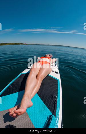 Femme se relaxant sur Paddleboard dans les eaux claires Banque D'Images