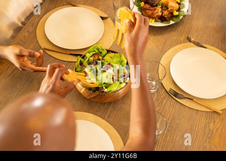 Servant une salade fraîche à la table du dîner familial, mains préparant le repas ensemble Banque D'Images
