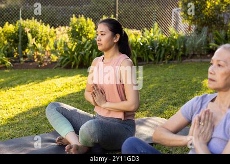 Pratiquer le yoga, grand-mère asiatique et petite-fille assise sur des tapis dans le jardin, méditer en plein air Banque D'Images