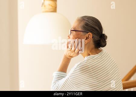 Contempler, femme asiatique âgée avec des lunettes assis sous la lampe, regardant réfléchi Banque D'Images