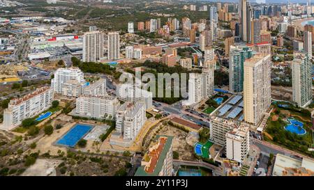 Vue aérienne drone au-dessus de la Cala (la Cala de Finestrat), un joyau côtier tranquille situé à une courte distance des gratte-ciel animés de Benidorm le long de la populaire Costa Blanca espagnole. La large plage de sable doré se courbe doucement dans les eaux turquoises calmes méditerranéennes, encadrées par des hôtels de faible hauteur, des appartements et des collines couvertes de pins. En arrière-plan, le célèbre horizon de Benidorm, composé de gratte-ciel imposants, contraste fortement avec l'ambiance détendue et familiale de la Cala. Un endroit idéal pour des journées paisibles à la plage, nager et profiter de la vue sur la côte depuis le belvédère voisin de Tossal de la Cala. Banque D'Images