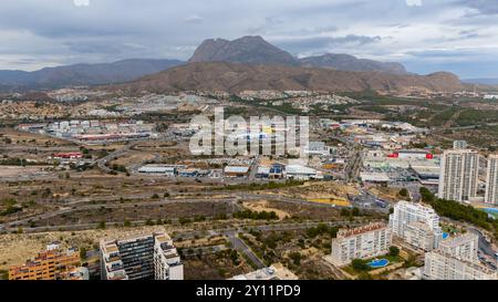 Vue aérienne drone au-dessus de la Cala (la Cala de Finestrat), un joyau côtier tranquille situé à une courte distance des gratte-ciel animés de Benidorm le long de la populaire Costa Blanca espagnole. La large plage de sable doré se courbe doucement dans les eaux turquoises calmes méditerranéennes, encadrées par des hôtels de faible hauteur, des appartements et des collines couvertes de pins. En arrière-plan, le célèbre horizon de Benidorm, composé de gratte-ciel imposants, contraste fortement avec l'ambiance détendue et familiale de la Cala. Un endroit idéal pour des journées paisibles à la plage, nager et profiter de la vue sur la côte depuis le belvédère voisin de Tossal de la Cala. Banque D'Images