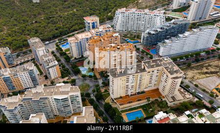 Vue aérienne drone au-dessus de la Cala (la Cala de Finestrat), un joyau côtier tranquille situé à une courte distance des gratte-ciel animés de Benidorm le long de la populaire Costa Blanca espagnole. La large plage de sable doré se courbe doucement dans les eaux turquoises calmes méditerranéennes, encadrées par des hôtels de faible hauteur, des appartements et des collines couvertes de pins. En arrière-plan, le célèbre horizon de Benidorm, composé de gratte-ciel imposants, contraste fortement avec l'ambiance détendue et familiale de la Cala. Un endroit idéal pour des journées paisibles à la plage, nager et profiter de la vue sur la côte depuis le belvédère voisin de Tossal de la Cala. Banque D'Images