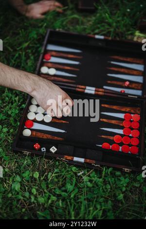 Main jouant au backgammon à l'extérieur sur l'herbe avec des dés et des morceaux Banque D'Images
