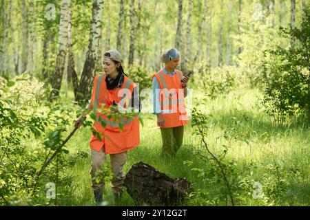 Jeunes et matures volontaires féminines ou sauveteurs en gilets réfléchissants orange acide se déplaçant le long de la forêt et à la recherche de touristes perdus Banque D'Images