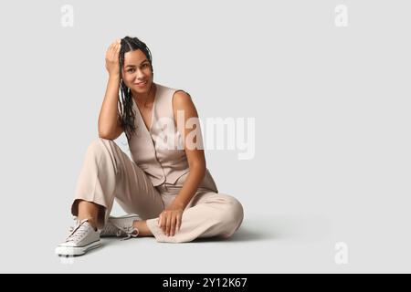 Belle jeune femme d'affaires afro-américaine avec des dreadlocks assis sur fond gris Banque D'Images