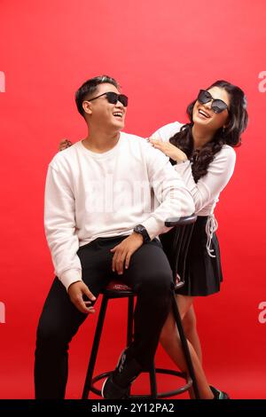 Un jeune couple d'hommes et de femmes indonésiens riant portant des chandails blancs, des lunettes de soleil, tous deux racontant des histoires drôles et riant à haute voix. pour romance, Banque D'Images