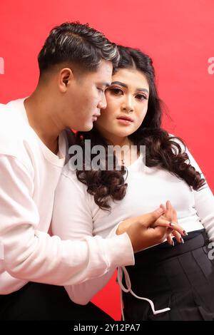 Un jeune couple, un joyeux homme asiatique et une femme portant des chandails blancs, la femme s'appuyant affectueusement contre l'homme en regardant vers l'avant. pour roman Banque D'Images