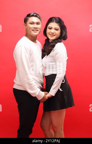 souriant jeune couple indonésien portant des chandails blancs debout face à face se tenant la main. pour romance, mariage, publicité, contenu promotionnel Banque D'Images