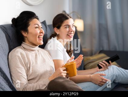 Deux amies qui regardent la télévision tout en étant assise sur un canapé à la maison Banque D'Images