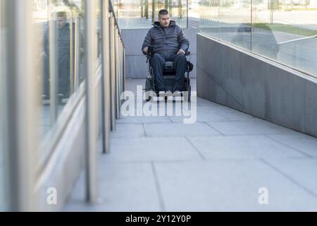 Homme en fauteuil roulant à l'aide d'une rampe à côté d'escaliers Banque D'Images