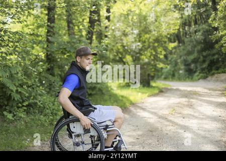 Professionnels et jeunes handicapés homme assis sur un fauteuil roulant dans la nature les roues en rotation sur une route à pied à une belle journée ensoleillée Banque D'Images