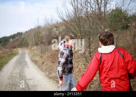 Deux jeunes hommes se promènent sur un chemin de gravier, riant et s'engageant les uns avec les autres, entourés d'arbres et de champs ouverts sous un ciel lumineux. Banque D'Images