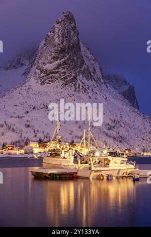 Bateaux de pêche dans le fjord devant les montagnes enneigées, illuminé, crépuscule, hiver, Reine, Moskenesoya, Lofoten, Norvège, Europe Banque D'Images