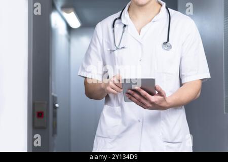 Photo d'un médecin masculin en uniforme avec stéthoscope sortant de l'ascenseur et utilisant une tablette informatique à l'hôpital. Concept médical moderne Banque D'Images