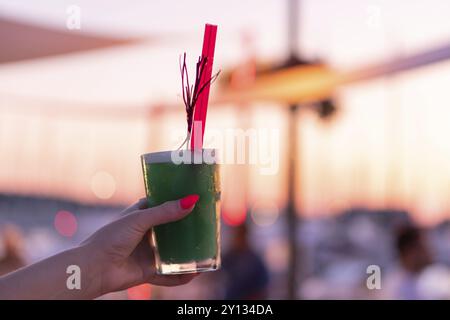 Woman's hand holding a cocktail glass contre le soleil couchant avec arrière-plan flou Banque D'Images