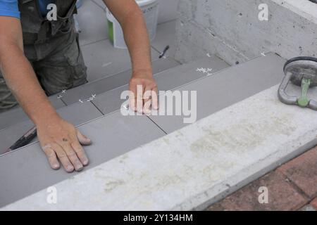 Mains de carrelage travaillant sur une nouvelle entrée de maison, bricoleur local et professionnel appliquant des carreaux sur les marches Banque D'Images