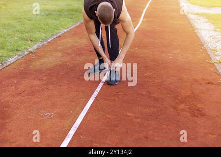 Jeune homme chaussures de liage de la préparation pour le jogging le matin en plein air, sur la voie de course course Banque D'Images