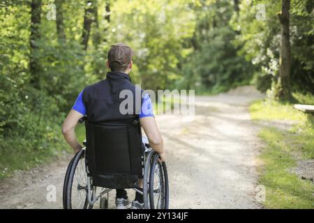 Professionnels et jeunes handicapés homme assis sur un fauteuil roulant dans la nature les roues en rotation sur une route à pied à une belle journée ensoleillée Banque D'Images