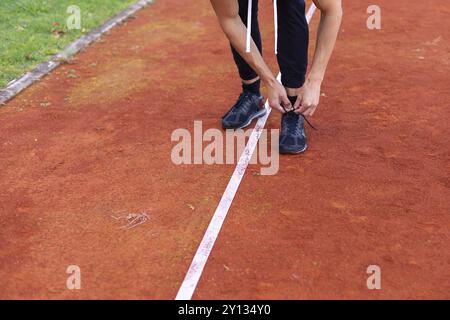 Jeune homme chaussures de liage de la préparation pour le jogging le matin en plein air, sur la voie de course course Banque D'Images