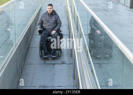 Homme en fauteuil roulant à l'aide d'une rampe à côté d'escaliers Banque D'Images