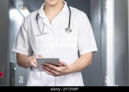 Photo d'un médecin masculin en uniforme avec stéthoscope sortant de l'ascenseur et utilisant une tablette informatique à l'hôpital. Concept médical moderne Banque D'Images