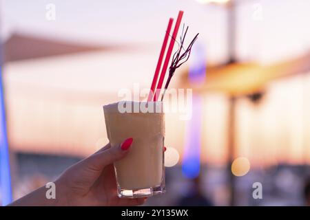 Woman's hand holding a cocktail glass contre le soleil couchant avec arrière-plan flou Banque D'Images