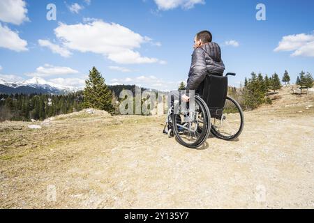 Jeune homme handicapé en fauteuil roulant à l'extérieur dans la nature l'observation de montagne et la nature Banque D'Images