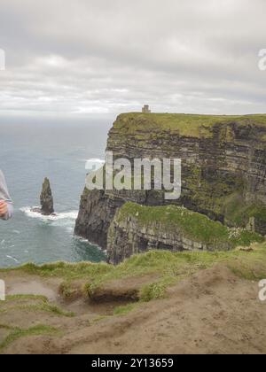 Les imposantes falaises avec une petite tour au sommet et une verdure luxuriante s'étendent vers la mer sous un ciel nuageux, falaises de moher, atlantique, irlande Banque D'Images