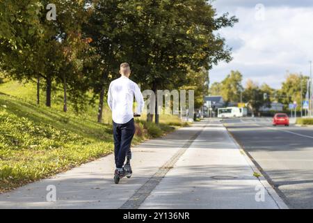 Joyeux et casual man riding scooter électrique dans le parc de la ville Banque D'Images