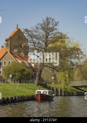 Un canal avec un petit bateau, bordé d'arbres à côté d'une vieille tour et de maisons au printemps, haarlem, pays-Bas Banque D'Images