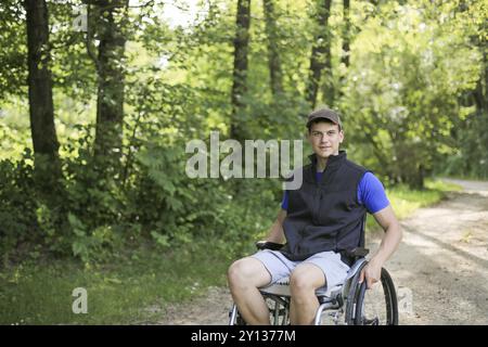 Professionnels et jeunes handicapés homme assis sur un fauteuil roulant dans la nature les roues en rotation sur une route à pied à une belle journée ensoleillée Banque D'Images