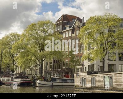 Façades de construction le long d'un canal avec des bateaux dans l'eau, entourées d'arbres verts et d'un ciel nuageux, Amsterdam, pays-Bas Banque D'Images