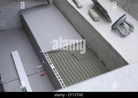 Mains de carrelage travaillant sur une nouvelle entrée de maison, bricoleur local et professionnel appliquant des carreaux sur les marches Banque D'Images