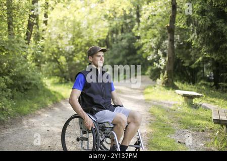 Professionnels et jeunes handicapés homme assis sur un fauteuil roulant dans la nature les roues en rotation sur une route à pied à une belle journée ensoleillée Banque D'Images