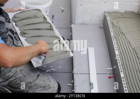 Mains de carrelage travaillant sur une nouvelle entrée de maison, bricoleur local et professionnel appliquant des carreaux sur les marches Banque D'Images