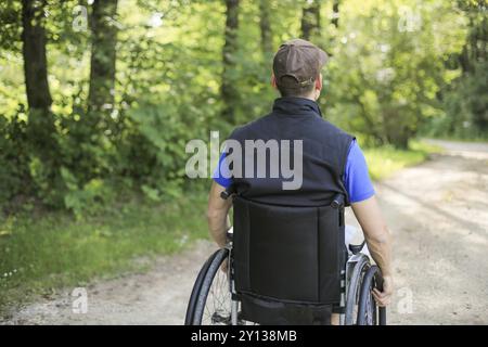 Professionnels et jeunes handicapés homme assis sur un fauteuil roulant dans la nature les roues en rotation sur une route à pied à une belle journée ensoleillée Banque D'Images