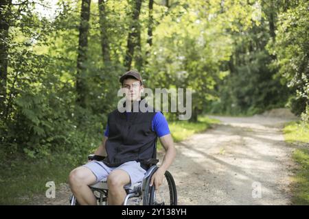 Professionnels et jeunes handicapés homme assis sur un fauteuil roulant dans la nature les roues en rotation sur une route à pied à une belle journée ensoleillée Banque D'Images