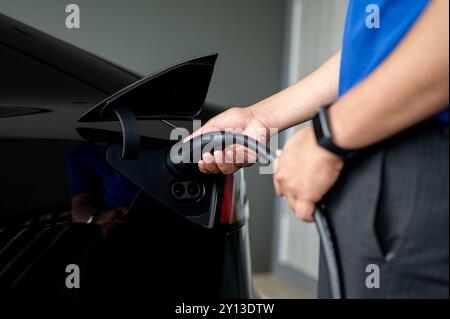 Une image en gros plan d'un homme insérant un câble de recharge dans sa voiture électrique à la maison, la chargeant avant de voyager. technologie verte, vie durable Banque D'Images