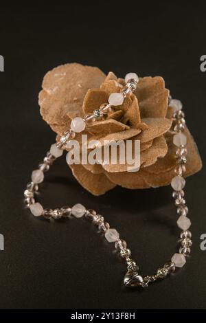 Collier de quartz rose clair et blanc avec un coeur métallique sur pierre rose du désert sur fond noir Banque D'Images