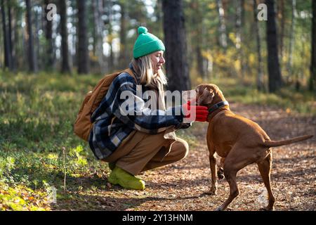 Femme joyeuse se penchant, discutant avec le chien, apaisant, caressant animal sur la promenade en forêt d'automne Banque D'Images