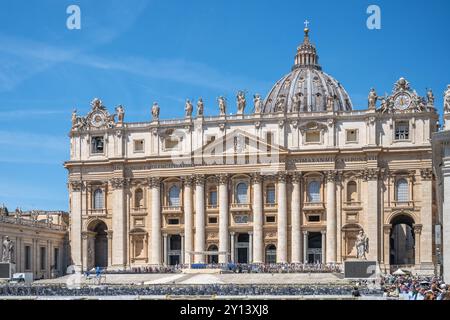 Les visiteurs admirent l'architecture étonnante de la basilique Saint-Pierre. La grande structure, ornée de sculptures, brille sous un ciel bleu vif, attirant des touristes du monde entier. Banque D'Images