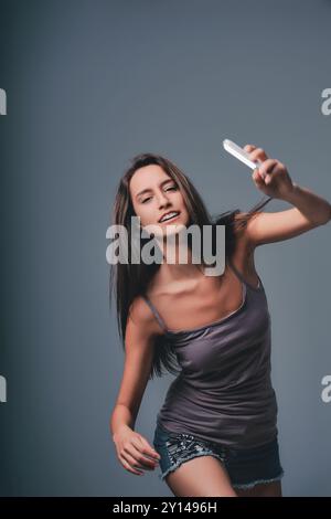 Joyeuse jeune femme prend un selfie avec son smartphone dans un studio, rayonnant de bonheur et de confiance Banque D'Images