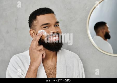 Un homme applique des soins de la peau tout en souriant dans une salle de bain lumineuse et moderne. Banque D'Images