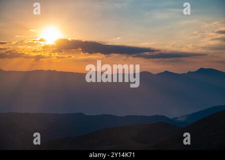 Le soleil couchant sur les montagnes, les beaux rayons du soleil brillent à travers les nuages, le fond naturel, la liberté, la tranquillité et la paix Banque D'Images