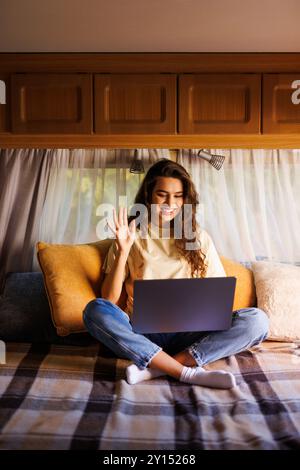 Jeune femme ayant un appel vidéo sur l'ordinateur portable à l'intérieur de sa camionnette de camping. Vacances en minibus et aventure en plein air en été. Concept de style de vie nomade Banque D'Images
