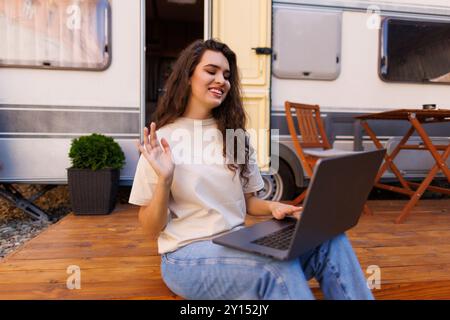 Une heureuse femme agite en regardant la caméra lors d'un appel vidéo depuis son fourgon de camping Banque D'Images